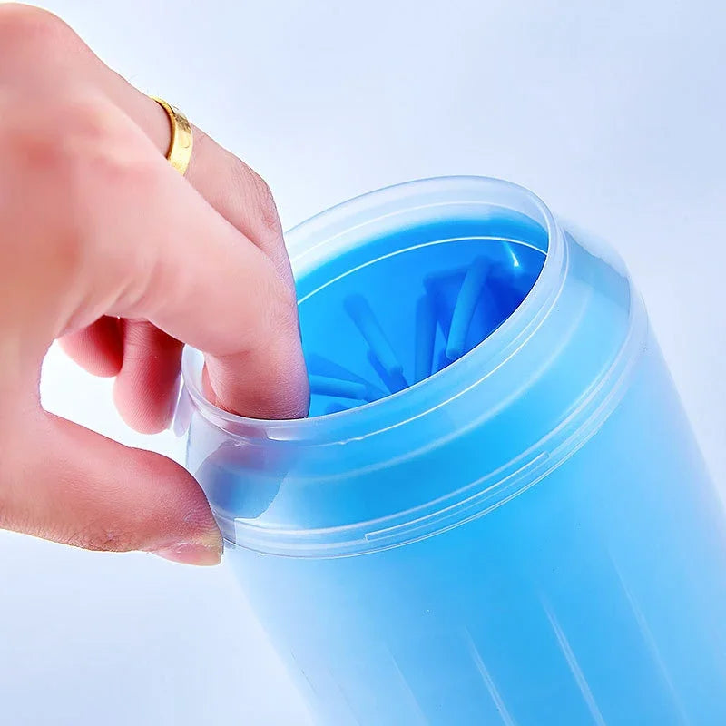 Hand opening a blue soft silicone pet paw cleaner with a white background