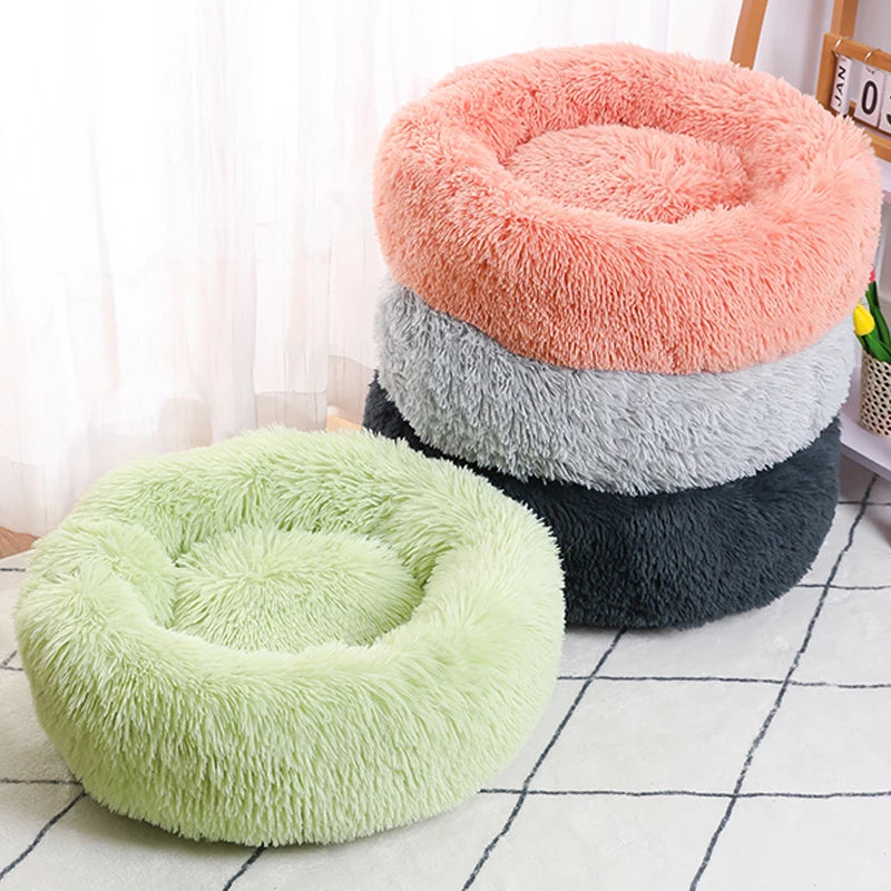 Three fluffy pet beds in pink, gray, and green on a white floor.