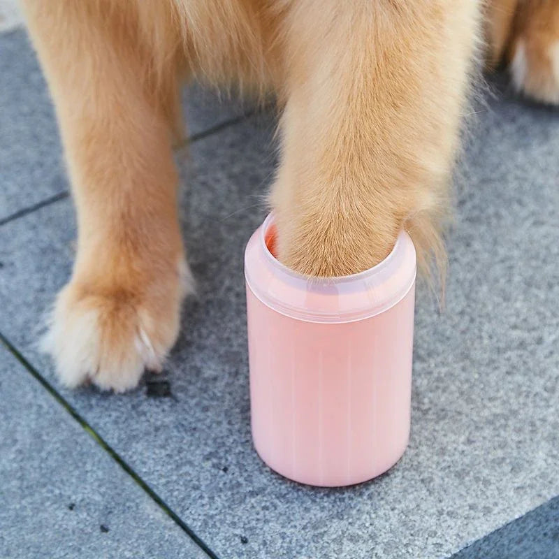 Dog paw in a pink soft silicone pet paw cleaner on a concrete surface